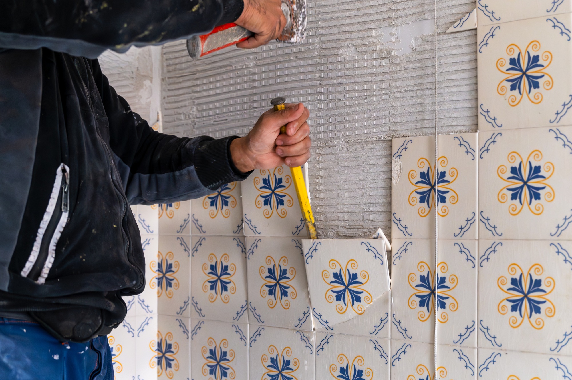 Construction worker removing old tiles from bathroom wall during renovation